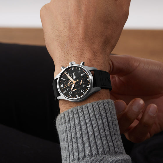 A person wearing a black wristwatch with a black rubber strap and a black dial, dressed in a gray sweater.
